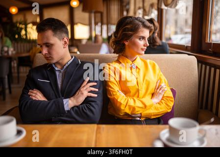 Unzufriedenes Paar sitzt Rücken an Rücken mit verschränkten Armen in einem Café Stockfoto