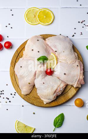 Rohe Hähnchenschenkel mit Gemüse auf einem Holzbrett, auf weißem Hintergrund. Stockfoto