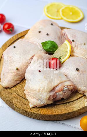 Rohe Hähnchenschenkel mit Gemüse auf einem Holzbrett, auf weißem Hintergrund. Stockfoto