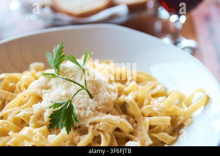 Köstliche hausgemachte Carbonara-Pasta, serviert in einer weißen Schüssel, garniert mit geriebenem Parmesan und frischer Petersilie in einer Restaurant-Atmosphäre. Stockfoto