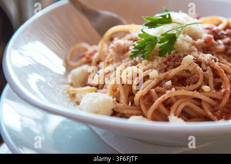 Nahaufnahme von köstlichen Spaghetti Bolognese, serviert in einer weißen Schüssel, großzügig mit geriebenem Käse überzogen und mit frischen grünen Petersilienblättern garniert Stockfoto