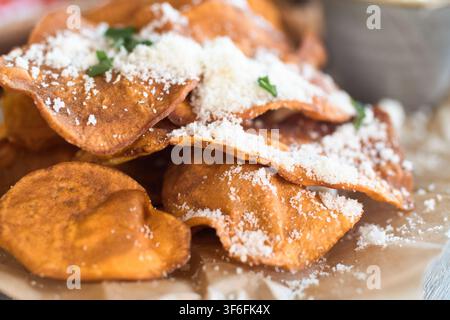 Nahaufnahme von knusprigen hausgemachten Süßpotato-Chips, garniert mit frisch geriebenem Parmesan und gehackten grünen Petersilienblättern. Stockfoto