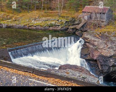 Tråo, Lærdal, Norwegen – 27.10.2016: Ein kleiner Damm lässt rauschendes Weißwasser in einen felsigen Bach neben einer alten verwitterten Holzhütte im Herbst fließen Stockfoto