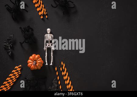 Oberansicht von Halloween-Dekorationen mit Skelett, Kürbis, Spinnen, Fledermäusen und Papierschnickseln, die auf schwarzem Hintergrund arrangiert sind, mit Kopierraum für saisonale Des Stockfoto