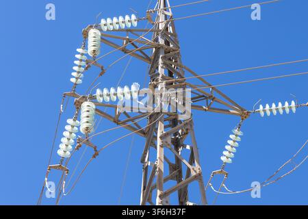 Nahaufnahme einer Metall-Hochspannungsmaststruktur, die Leitungsnetze mit mehreren Glasisolatoren trägt Stockfoto