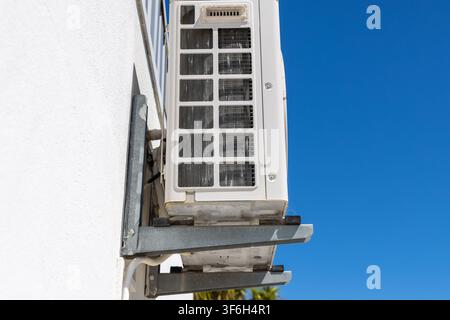 Eine Nahaufnahme einer externen Klimaanlage, die ihre Kondensatorlamellen und die Befestigungsklammer vor einem hellen, wolkenlosen Himmel zeigt Stockfoto