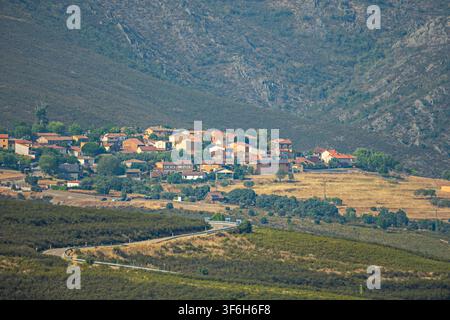 Traditionelles Steindorf mit Terracotta-Dächern liegt unterhalb eines schroffen Berghangs, eine kurvenreiche Straße führt durch die Landschaft Stockfoto