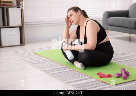 Müde übergewichtige Frau auf Fitnessmatte zu Hause, Platz für Text Stockfoto