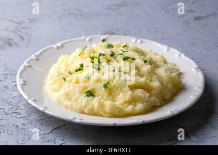 Cremige hausgemachte Kartoffelpüree, garniert mit gehackter frischer Petersilie, serviert auf einem weißen Teller über grauem Betonhintergrund Stockfoto