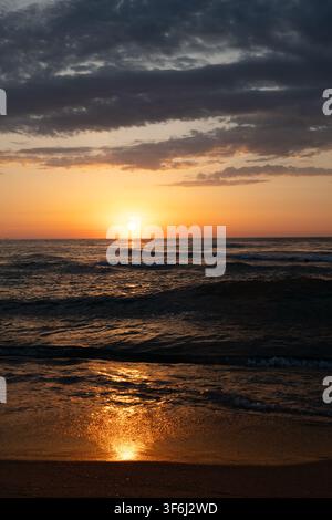Goldener Sonnenaufgang über dem Meer mit dramatischen Wolken und Reflexionen am Strand Stockfoto