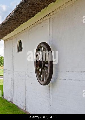 Vordingborg, Dänemark - 31.07.2017: Rustikales altes Holzrad, das an einer strukturierten weißen Kalkwand eines historischen dänischen Hauses mit Strohdach montiert ist Stockfoto