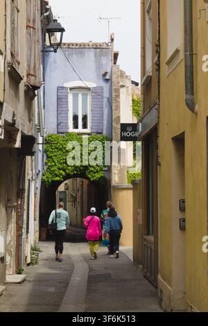Fußgänger gehen eine schmale Straße in L'Isle-sur-la-Sorgue, Frankreich, entlang. Stockfoto