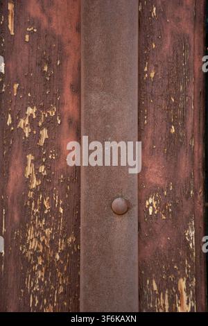 Vertikale Textur eines rostigen Eisenbalkens auf altem Holz mit abblätternder roter Farbe Stockfoto