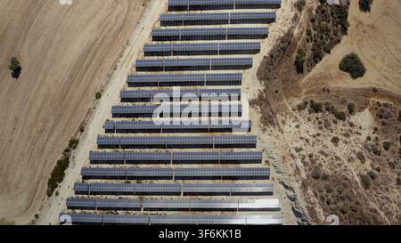 Reihen von Solarmodulen, die auf einem trockenen Hügel in Zypern installiert sind, fangen Sonnenlicht ein, um saubere Elektrizität zu erzeugen und tragen zur nachhaltigen Energieentwicklung bei. Luftaufnahme von oben, Drohnenflug Stockfoto