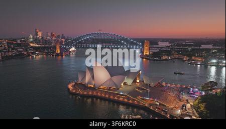 Sydney, Australien - 01.24.2023: Sydney Opera House mit der Sydney Harbour Bridge im Hintergrund, die nächtlichen Lichter beleuchtet, Stadtansicht mit farbenfrohem Himmel und beleuchteten Gebäuden. Drohnenaufnahmen aus der Luft Stockfoto