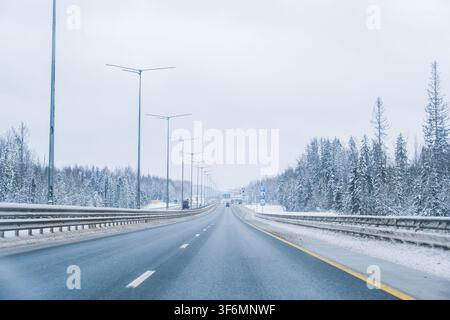 Russland, Sankt Petersburg, 11.01.2026 Straße, die sich durch einen schneebedeckten Winterwald schlängelt, mit Autos, die an einem kalten Dezembertag fahren. Kaltes Wetter dr Stockfoto