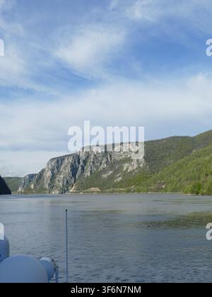 Donaufluss, der sich durch die Eisentore-Schlucht in Rumänien schneidet, mit hoch aufragenden bewaldeten Bergen und felsigen Klippen unter einem blauen Himmel, reflektierendes Wasser, Showcasi Stockfoto