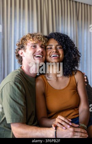 Paar sitzt auf dem Sofa zu Hause, Mann in olivfarbenem T-Shirt hält die Hände einer afroamerikanischen Frau. Romantik, Zuneigung, gemütlich, intim, warm, Vorhänge, Armband Stockfoto