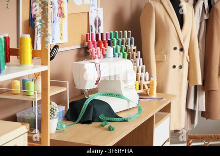 Moderner Schneiderarbeitsplatz mit Garnspulen, Nähmaschine und Maßband im Atelier Stockfoto