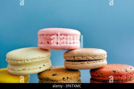 Bunte französische Macarons stapeln sich in einer Pyramide vor blauem Hintergrund. Berühmte Weet-Dessertbäckerei, Makrodetail-Fotografie von Lebensmitteln, lebhafte Pastellfarben Stockfoto