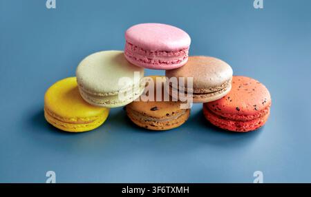 Bunte französische Macarons stapeln sich in einer Pyramide vor blauem Hintergrund. Berühmte Weet-Dessertbäckerei, Makrodetail-Fotografie von Lebensmitteln, lebhafte Pastellfarben Stockfoto