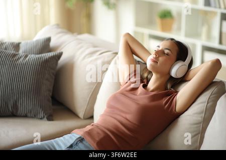 Frau mit Kopfhörern sitzt entspannt auf einer Couch zu Hause Stockfoto