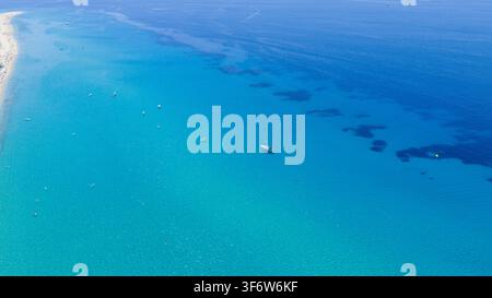 Mehrere kleine Boote treiben über klare türkise Flachwasserzonen in der Nähe des Strandes von Possidi, während dunklere Unterwasserflecken und tiefblaues Offenen Wasser sich in Richtung t erstrecken Stockfoto