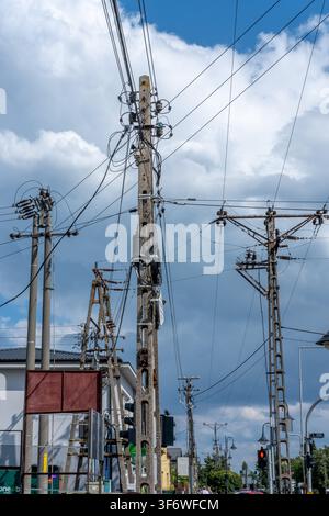 Betongrundstützen stützen verworrene Stromkabel vor einem wolkigen blauen Himmel in einer städtischen Umgebung. Stockfoto
