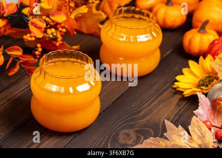 Saisonaler Apfelsaft oder -nektar in zwei einzigartigen Glasbehältern. Umgeben von Herbstblättern. Beeren. Und dekorative Kürbisse auf dunklem Holzgrund. Stockfoto