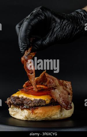 Koch fügt eine Scheibe knusprig gebratenen Specks zu einem Gourmet-Burger hinzu Stockfoto