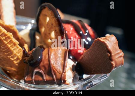Eine Nahaufnahme eines reichhaltigen und cremigen Eisbechers, der mit glattem Schokoladensirup, knusprigen Waffeln und süßen Leckereien in einer Glasschale serviert wird. Stockfoto