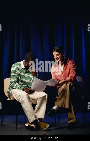 Schwarzer Mann und Frau sitzen auf Stühlen und lesen ein Skript im Schauspielunterricht Stockfoto