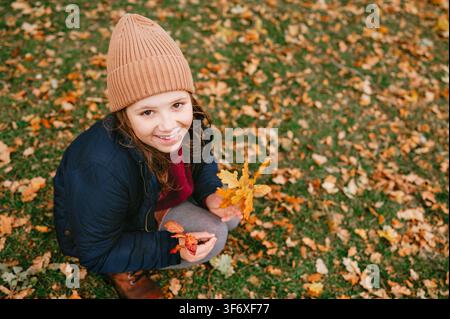 Fröhliches Mädchen schaut nach oben und hält bunte Herbstblätter Stockfoto