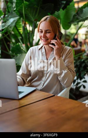 Glückliche Frau arbeitet an einem Laptop und nimmt einen Anruf entgegen Stockfoto
