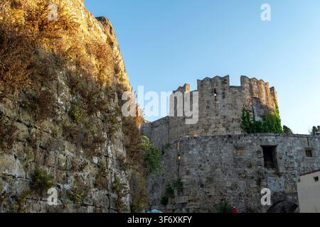 Eine große Steinmauer des Palastes des Großmeisters der Ritter von Rhodos ist in hellem Licht zu sehen. Die Mauer hat viele Steine und einige Pflanzen wachsen Stockfoto