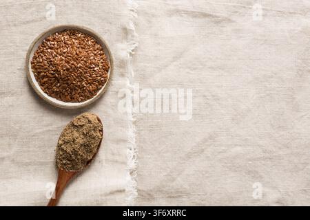 Leinsamen und Mehl in hölzernem Löffel und Schüssel auf Leinentischdecke. Ansicht von oben. Platz für Text. Stockfoto