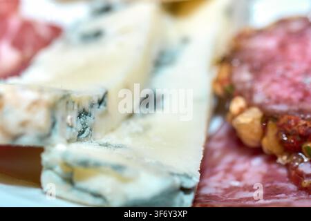 Nahaufnahme von verschiedenen geschnittenem Blauschimmelkäse mit Schimmeladern und einem Gourmet-Selchfleisch-Teller, serviert als Vorspeisen-Snack. Stockfoto