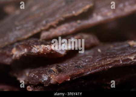 Makroaufnahme, die strukturierte Stücke getrockneten Beef Jerky mit sichtbaren Gewürzen und Würzmitteln zeigt, die gestapelt sind, um den handwerklich hergestellten gepökelten Fleischsnack zu präsentieren Stockfoto