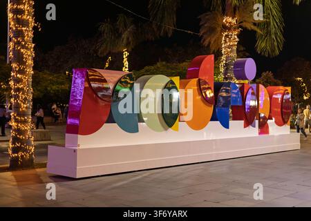 Funchal, Portugal - 05.12.2025: Moderne mehrfarbige kreisförmige Kunstinstallation auf einem weißen Podest unter den Abendlichtern der Stadt Stockfoto