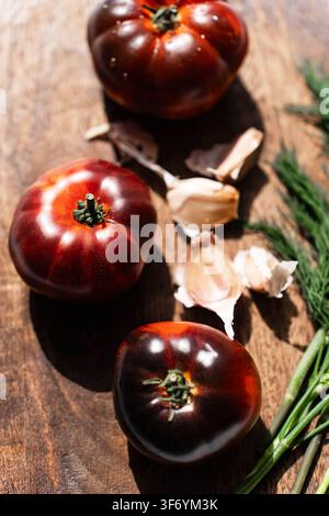Dunkle Heirloom-Tomaten mit Knoblauch und frischem Dill auf einem rustikalen Holzbrett. Oberansicht Stockfoto