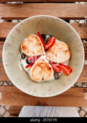Traditionelle Syrniki serviert mit cremiger Sauce, frischen Erdbeeren und Blaubeeren auf einem Keramikteller über einem Holztisch. Stockfoto