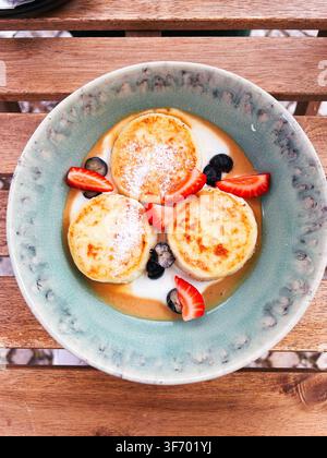 Traditionelle Syrniki-Käsepfannkuchen serviert mit cremiger Karamellsoße, Erdbeeren und Blaubeeren Stockfoto