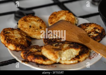 Goldbraune Hüttenkäse-Syrniki-Pfannkuchen, die auf einem Keramikgeschirr mit einem Spatel ruhen, die authentische Textur einer einfachen Morgenmahlzeit einfangend Stockfoto