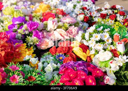 Eine Nahaufnahme von verschiedenen künstlichen Seidenblumen in verschiedenen brillanten Farbtönen bildet eine strukturierte Blumenausstellung, die für fröhliche Anlässe geeignet ist und kreat Stockfoto