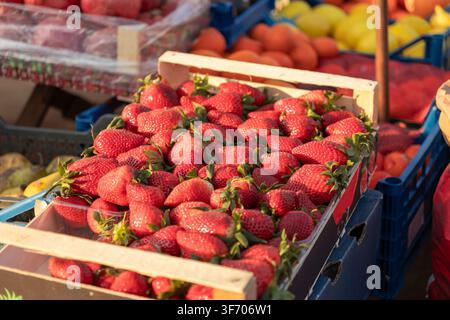 Nahaufnahme von reifen Erdbeeren, die in einer Holzkiste auf einem sonnigen Bauernmarkt verpackt sind, die lebendige landwirtschaftliche Fülle, saisonales Sommerobst illustrieren Stockfoto