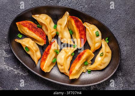 Knödel werden auf einem schwarzen Teller mit grüner Zieronion garniert in einer Kücheneinrichtung serviert Stockfoto