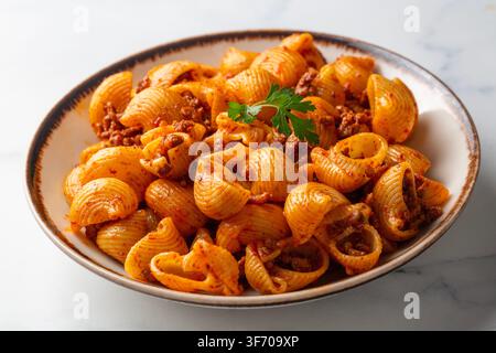 Blick von oben auf Conchiglie Shell Pasta mit Bolognese Fleischsauce und frischem Basilikum - Pipe Rigate (Manti makarna) Stockfoto