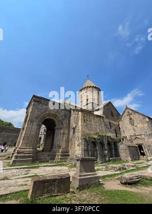 Armenische Tatev-Klosterruinen unter strahlend blauem Himmel. Verwitterte Mauern und Bögen ragen hoch mit grünem Moos. Sonnenlicht hebt die strukturierte Steinmetzarbeit hervor Stockfoto