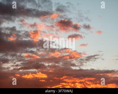 Dramatischer Sonnenuntergangshimmel mit orangefarbenen und rosa Wolken vor weichem blauem Hintergrund. Die Wolken bilden verstreute Flecken über dem Horizont Stockfoto