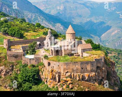 Altes Tatev-Kloster, das auf einer felsigen Klippenwand thront. Steinbauten mit kegelförmigen Dächern heben sich ab. Üppige grüne Täler erstrecken sich bis zu den fernen Bergen Stockfoto